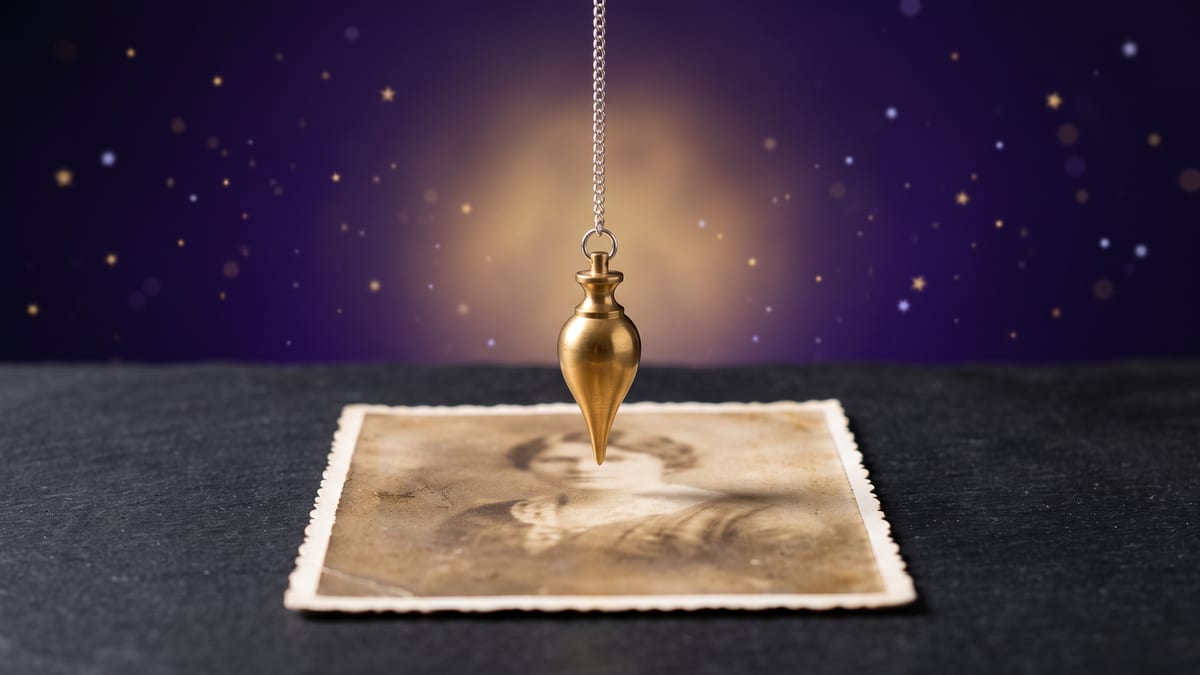 Pendule divinatoire en laiton doré suspendu immobile au-dessus d'une photographie ancienne posée à plat sur une table d'ardoise, fond violet étoilé