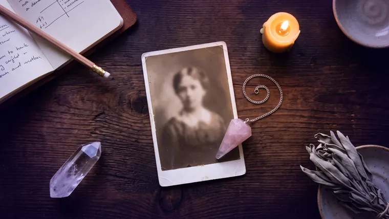 Espace de séance vu de dessus : photographie ancienne posée à plat, pendule en quartz rose, carnet, cristal de roche et bougie sur une table en bois sombre